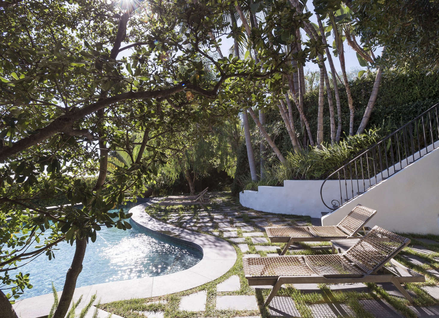 Black cantera stone pavers are set in a herringbone pattern and “grouted” with plugs of turf grass to create a permeable patio to surround a swimming pool in Los Angeles.