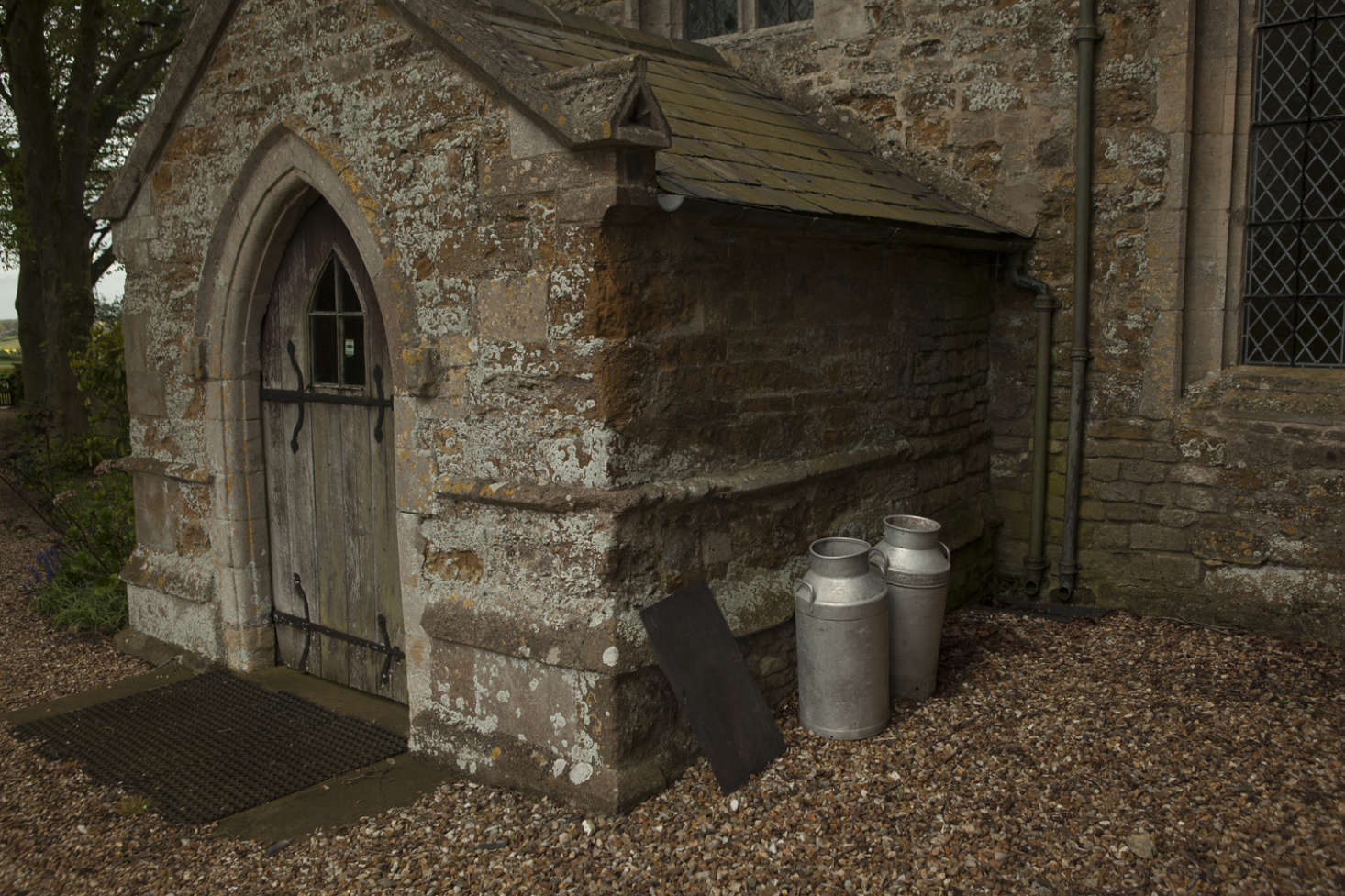 Milk churns by the porch of Saint Peter and Saint Paul, at Harrington, Northamptonshire.