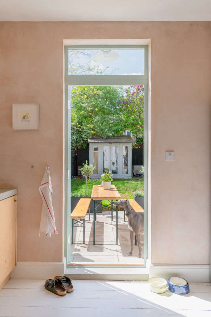 From inside, a view of the dining table and benches is framed by the open doorway. The small garden also has a storage shed at the edge of the property. Photograph courtesy of The Modern House.