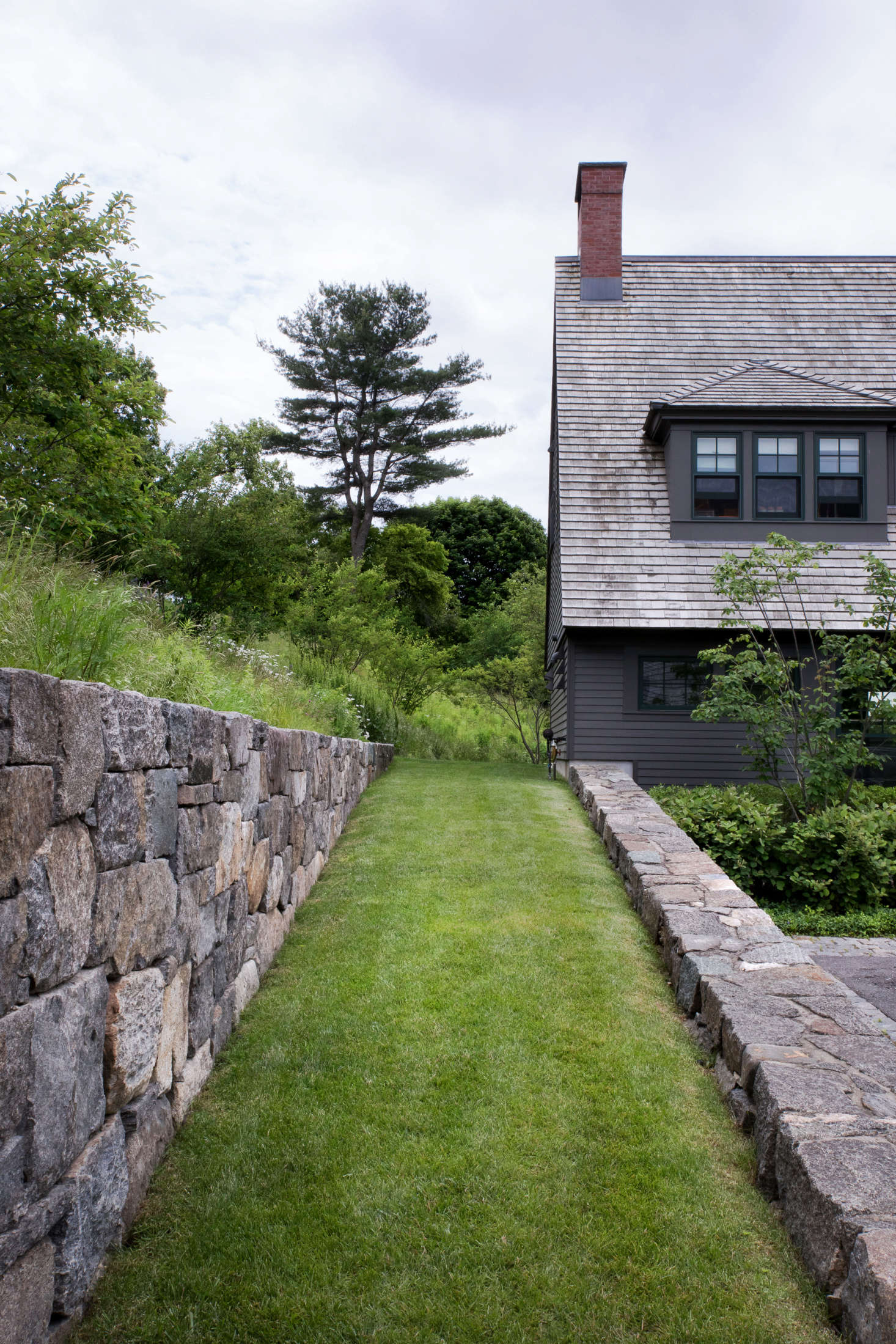 A lawn ramp, built with the type of large fieldstones typically used in farms, connects the entry level of the house to the upper outdoor living areas, where another retaining wall frames views of working farm fields. Mature trees were preserved whenever possible to help site the new construction and landscape within its setting. Visible in the distance is one of the largest pines found on the property, which was preserved and pruned.