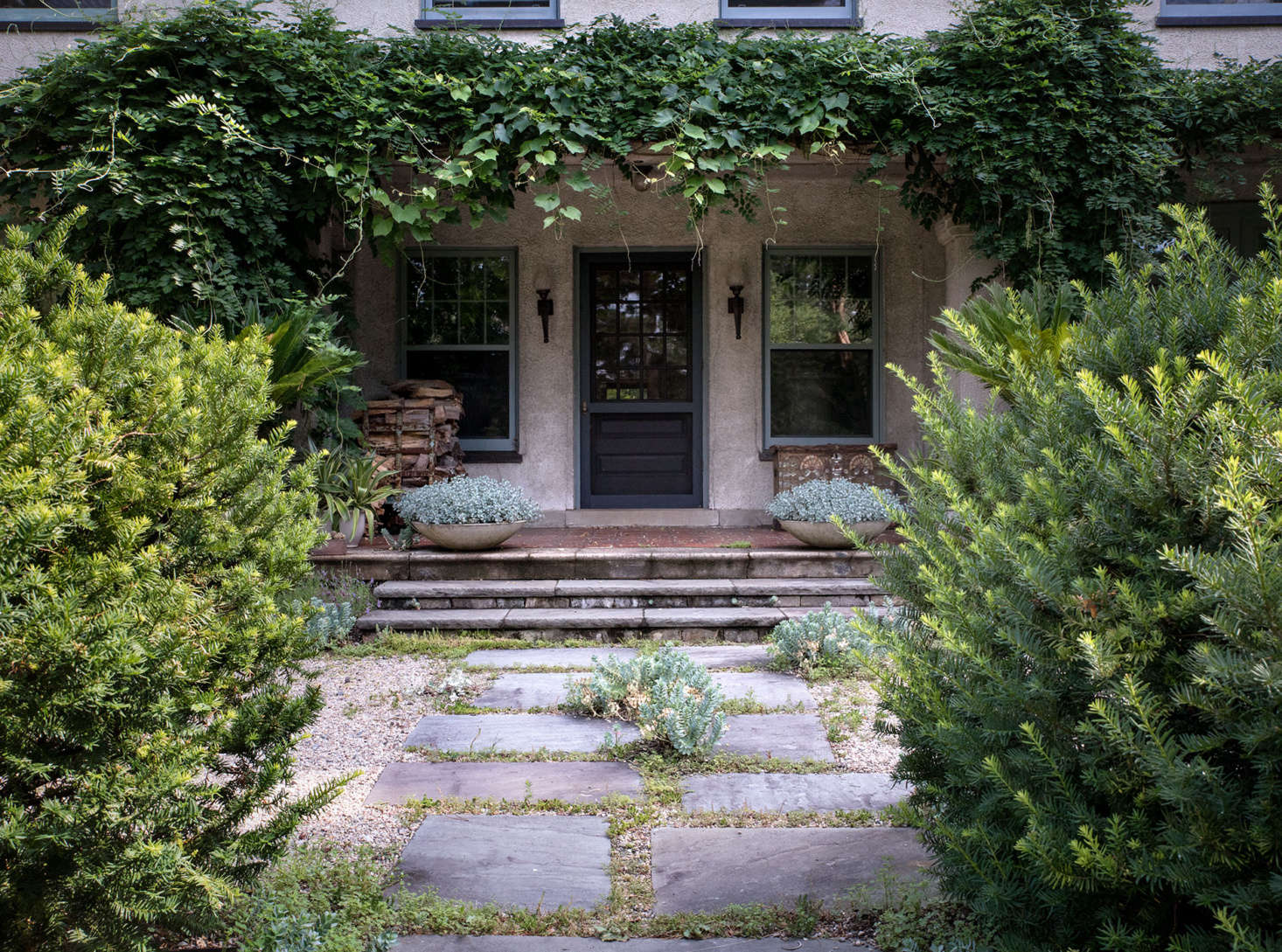 Framing a hand-hewn stone path, loosely shorn yews, as well as untamed vines and self-sewn plantings, conjure an atmosphere of old-world charm.