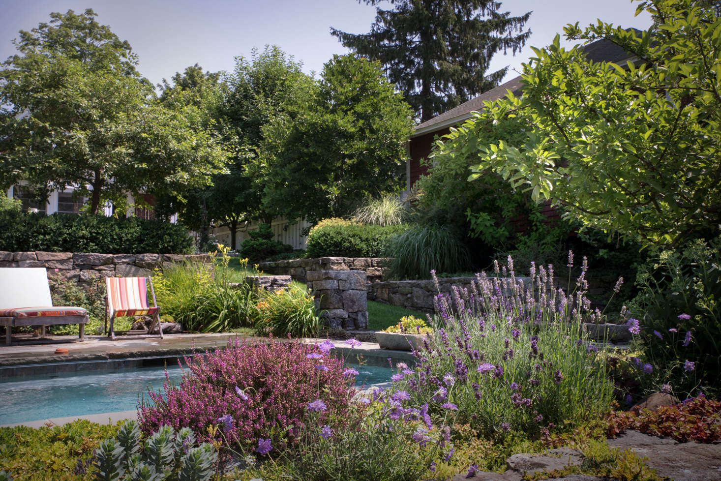 Hidden from the main house by a stone retaining wall and lush plantings, the plunge pool feels like a private oasis. A low rock garden on the opposite side provides an unobstructed view of the woods that abut the property.