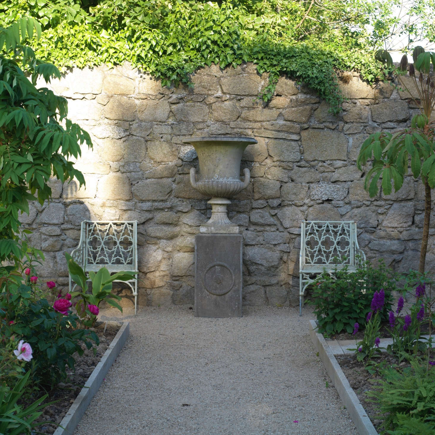 The symmetry of two chairs flanking an urn imposes order on the colorfully chaotic flower borders.